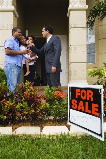 Hispanic real estate agent giving house keys to African family