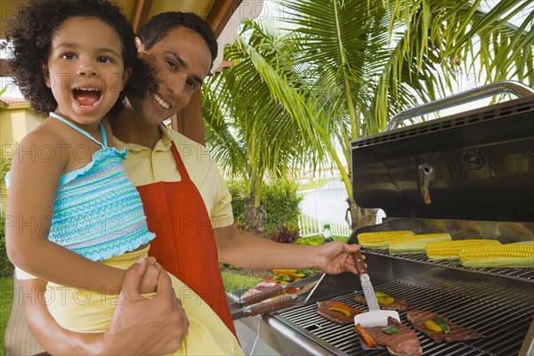 Hispanic father and daughter barbecuing