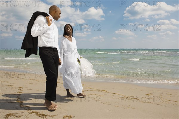 African bride and groom holding hands at beach