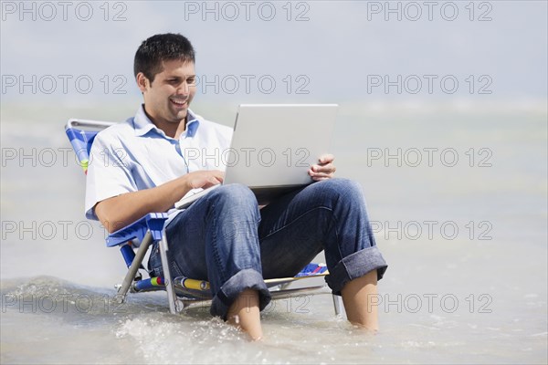 Hispanic man in beach chair with laptop