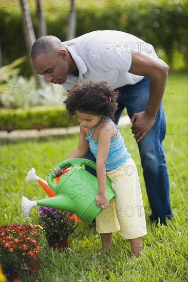 African father and daughter watering flowers