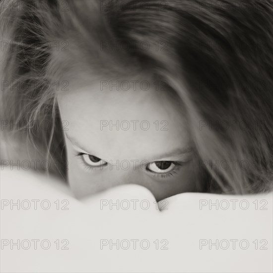 Caucasian girl peering over bed covers