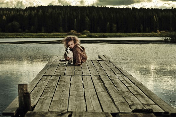 Caucasian girl with dog on wooden deck in still lake
