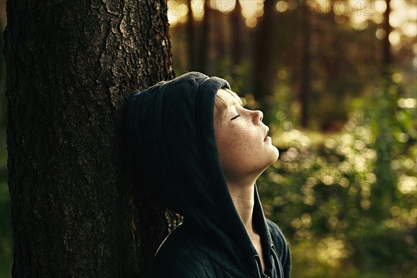 Caucasian boy leaning against tree