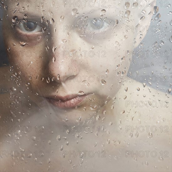 Caucasian woman peering through wet glass