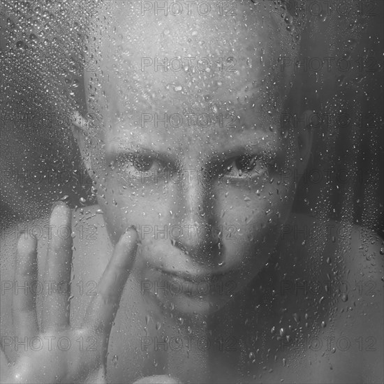 Caucasian woman peering through wet glass