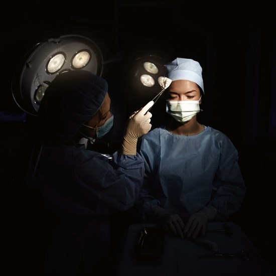 Caucasian nurse wiping sweat from surgeon's brow