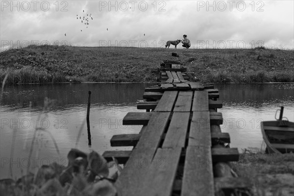 Girl petting dog near rustic wooden bridge crossing river