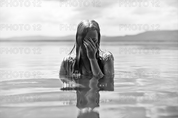 Caucasian teenage girl covering her face in lake