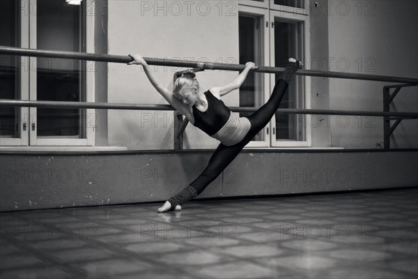 Caucasian dancer doing splits on barre in studio