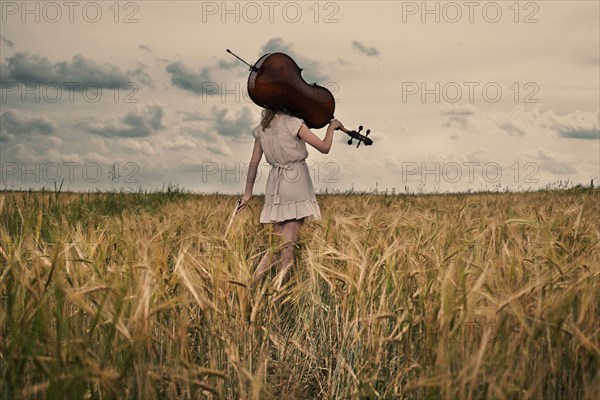 Caucasian girl carrying cello on shoulder in rural fieldCaption