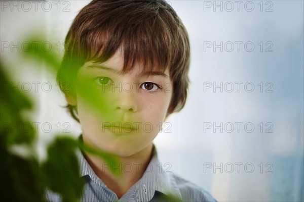 Caucasian boy standing behind plants indoors