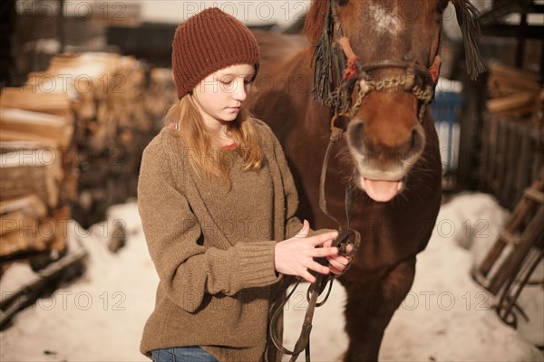 Caucasian teenage girl leading horse in snowy field