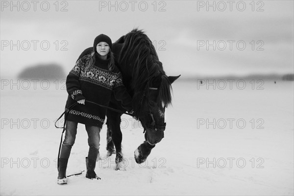 Caucasian teenage girl leading horse in snowy field