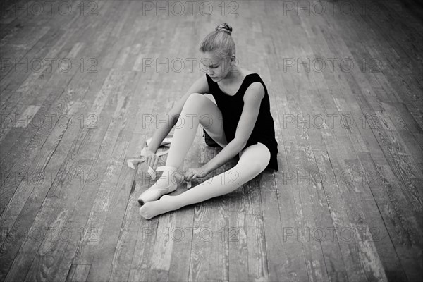 Caucasian ballerina tying pointe shoes