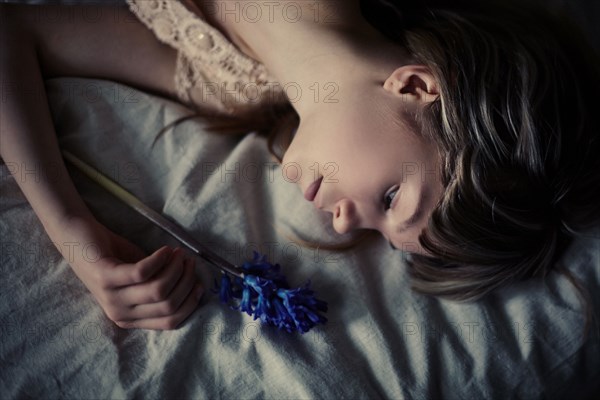 Caucasian teenage girl holding flower on bed