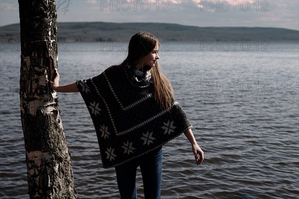 Caucasian girl leaning on tree trunk at lake