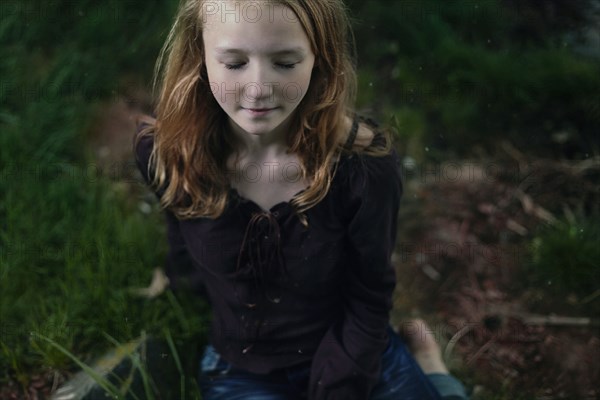 Caucasian girl sitting in grass with eyes closed