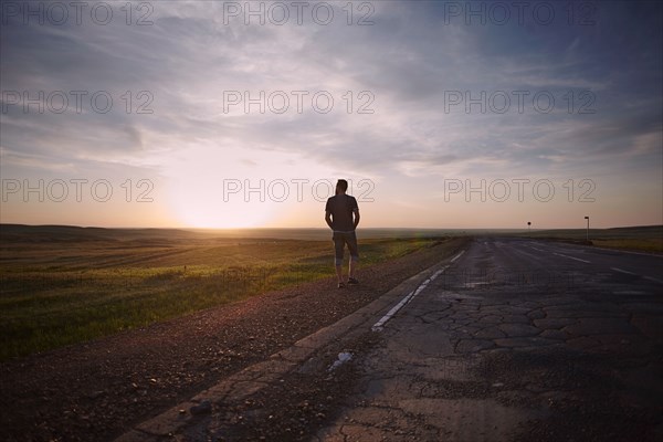 Caucasian man standing near cracked road at sunset