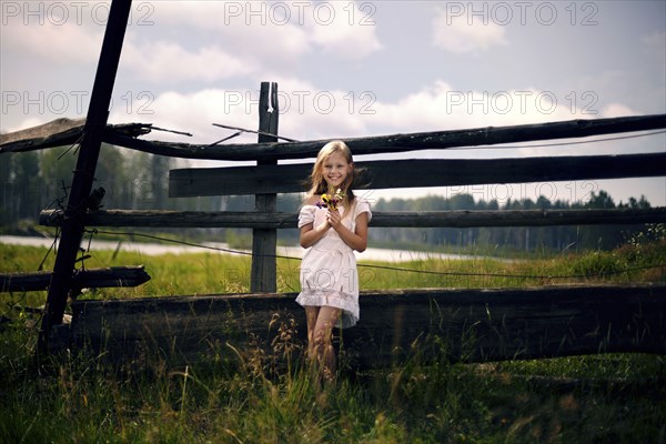 Caucasian girl holding bouquet of wildflowers leaning on wooden fence