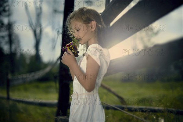 Caucasian girl smelling bouquet of wildflowers near wooden fence
