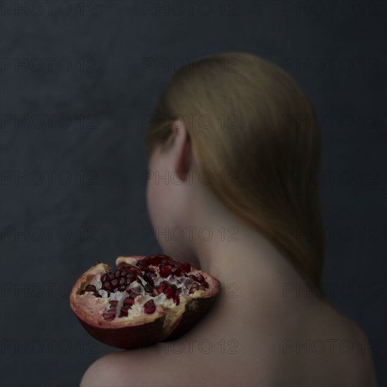 Caucasian girl balancing pomegranate slice on shoulder