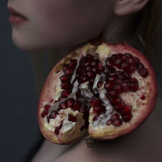 Caucasian girl balancing pomegranate slice on shoulder