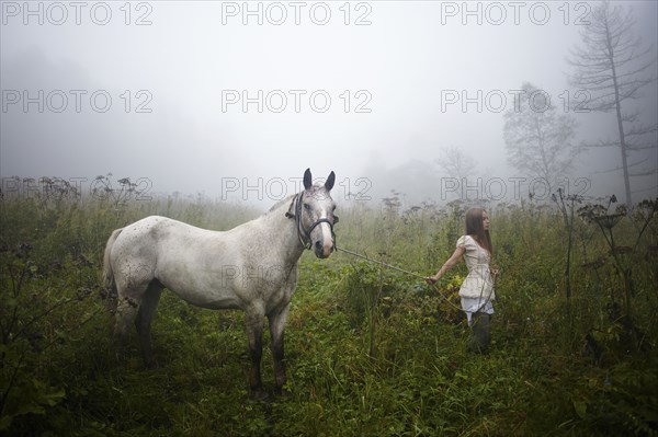 Caucasian girl walking horse in foggy field