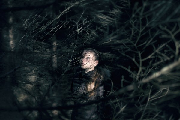 Caucasian teenage girl behind tree branches at night