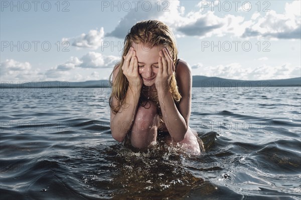 Caucasian teenage girl kneeling in ocean splashing water on face