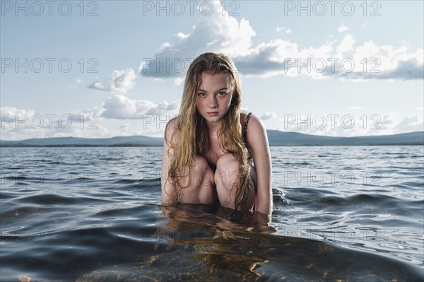 Caucasian teenage girl kneeling in ocean