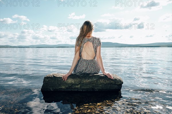 Caucasian teenage girl sitting on rock in ocean