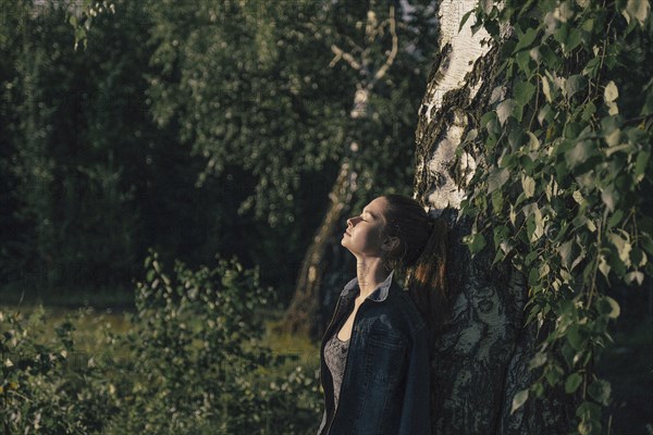 Caucasian woman leaning on tree trunk