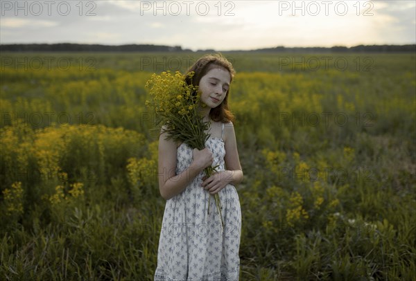 Caucasian girl standing in field holding bouquet of wildflowers