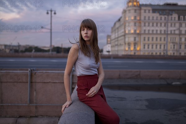 Serious Caucasian woman sitting on wall in city