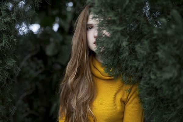 Serious Caucasian woman hiding behind tree