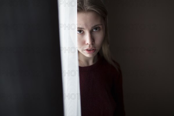 Serious Caucasian woman standing near curtain at window