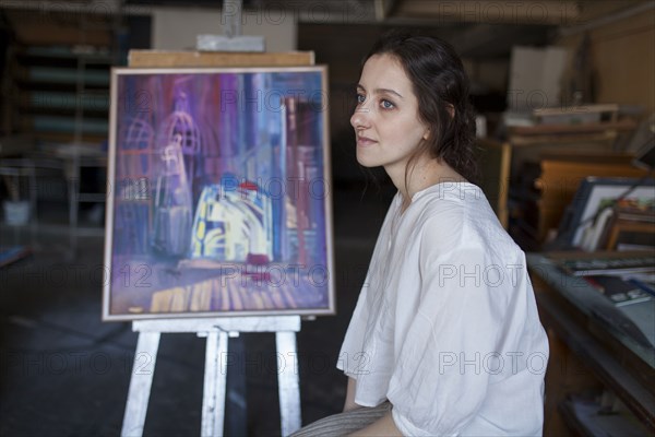 Caucasian artist sitting near paintings
