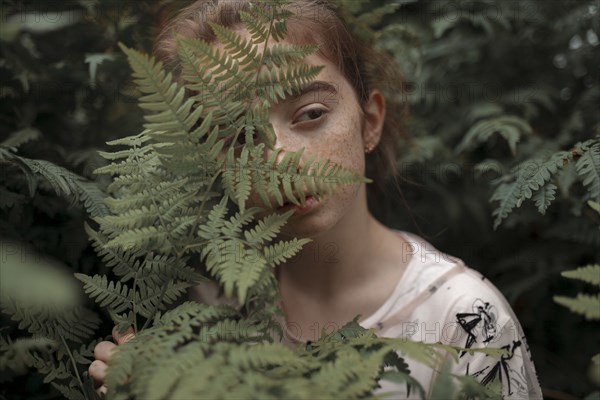 Pensive Caucasian girl behind green leaves