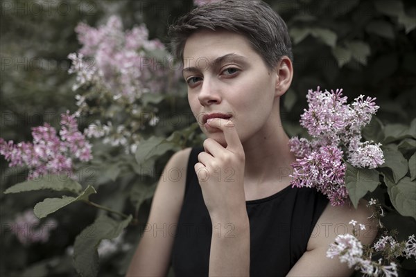 Curious Caucasian woman near flowering tree with finger on lip