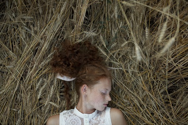Serious Caucasian girl with freckles laying in wheat