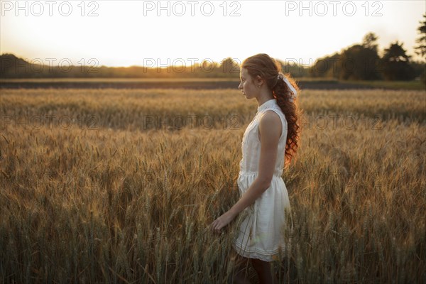 Pensive Caucasian girl standing in field of wheat