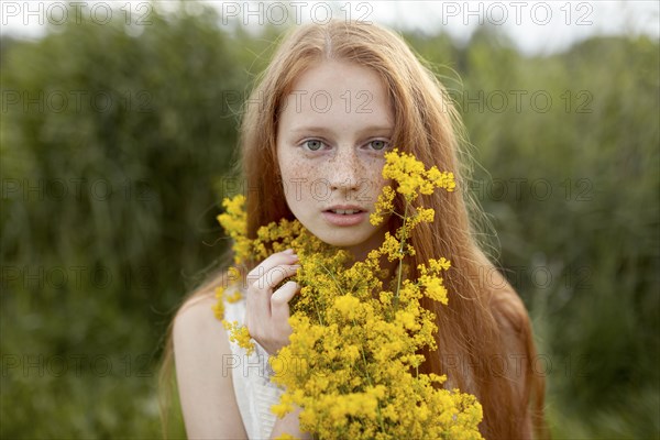 Portrait of serious Caucasian girl with freckles holding wildflowers