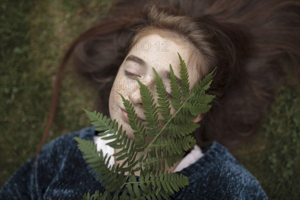 Caucasian girl laying in grass holding branch