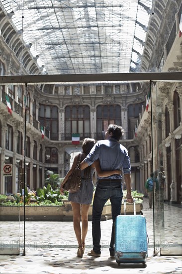 Caucasian couple pulling luggage into ornate building
