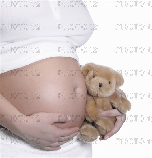 Caucasian woman holding teddy bear to pregnant belly