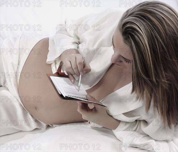 Pregnant Caucasian woman writing in planner