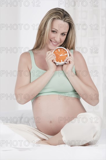 Pregnant Caucasian woman holding alarm clock