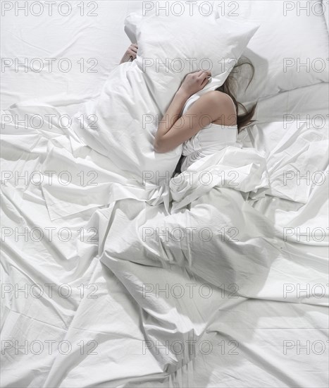Hispanic woman burying head under pillow
