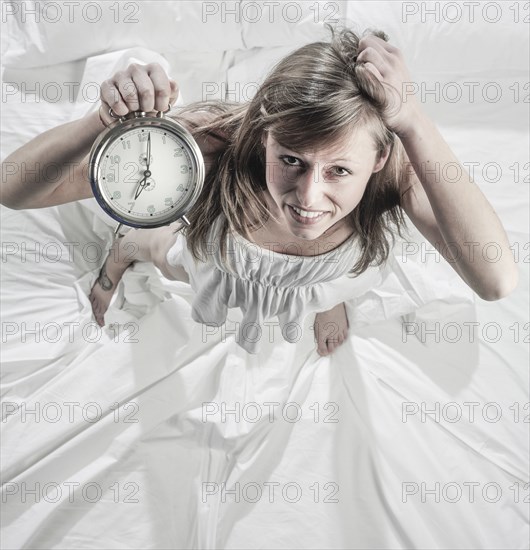 Hispanic woman holding alarm clock in bed